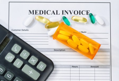 Close up overhead angled shot of bottle of pills, calculator and medical invoice